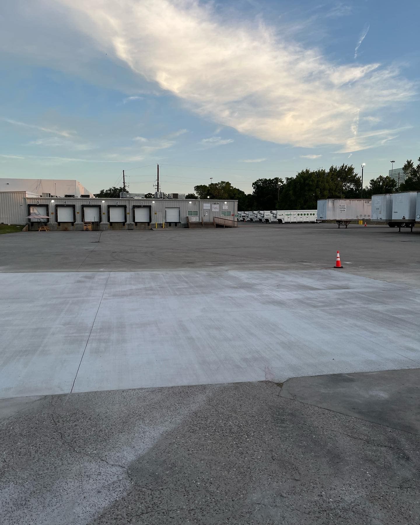 Empty loading dock area with blue sky and clouds; a single orange cone is in the center.