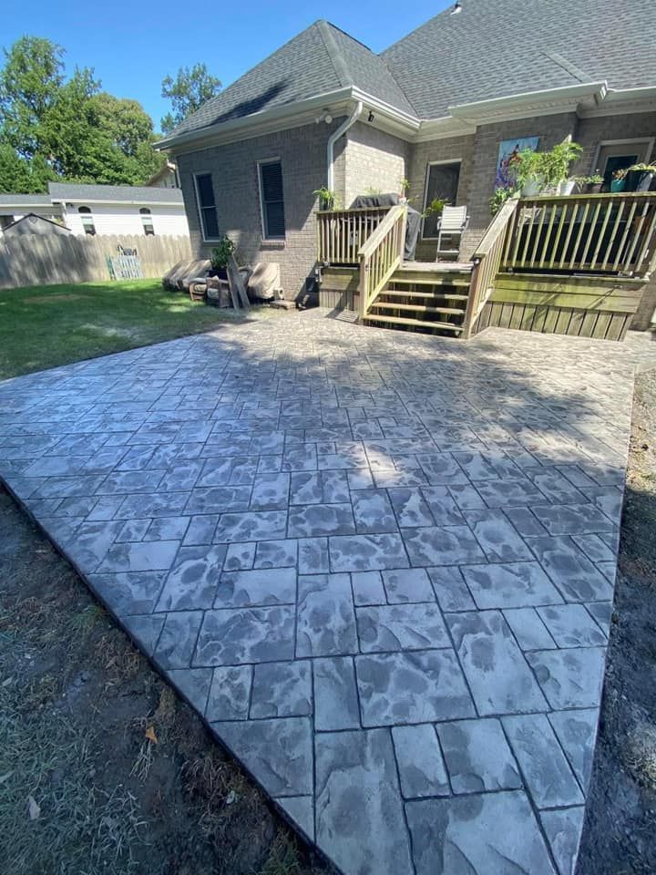 Stamped concrete patio next to a house with a deck; gray-toned, stone-like pattern.