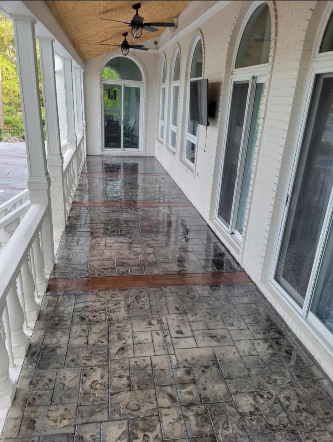 Covered porch with textured concrete floor, arched windows, and ceiling fans.