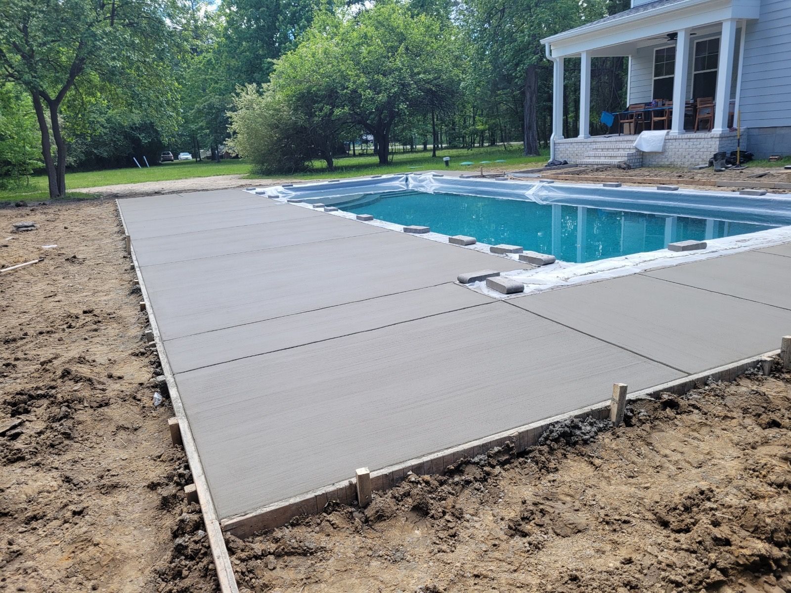 Newly poured concrete patio around a swimming pool, outdoors, on a sunny day.
