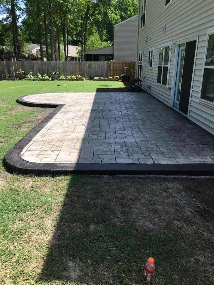 Brick patio with dark border in a backyard, next to a light-colored house.