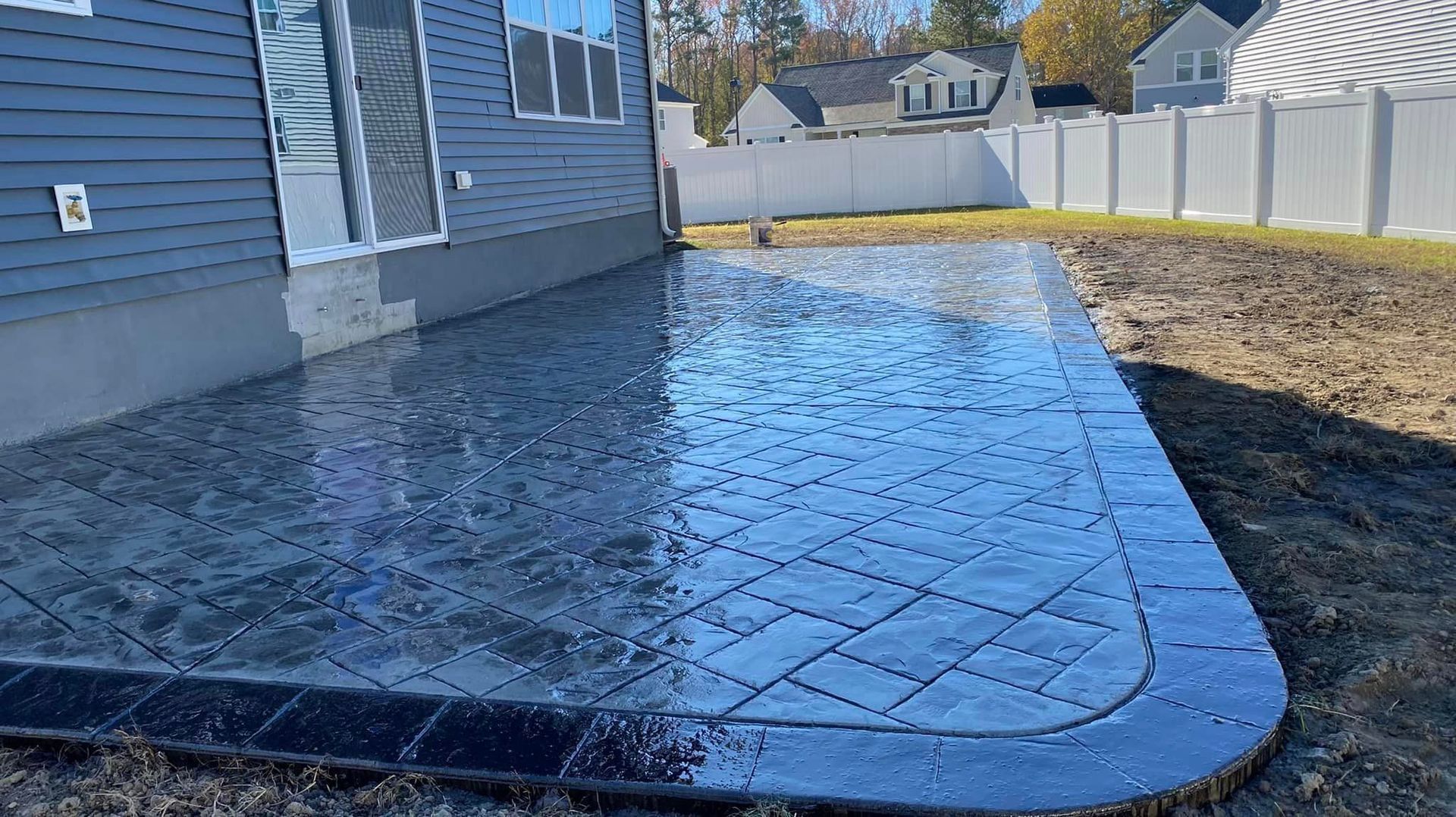 Exterior view of a dark gray stamped concrete patio with a contrasting black border next to a house.