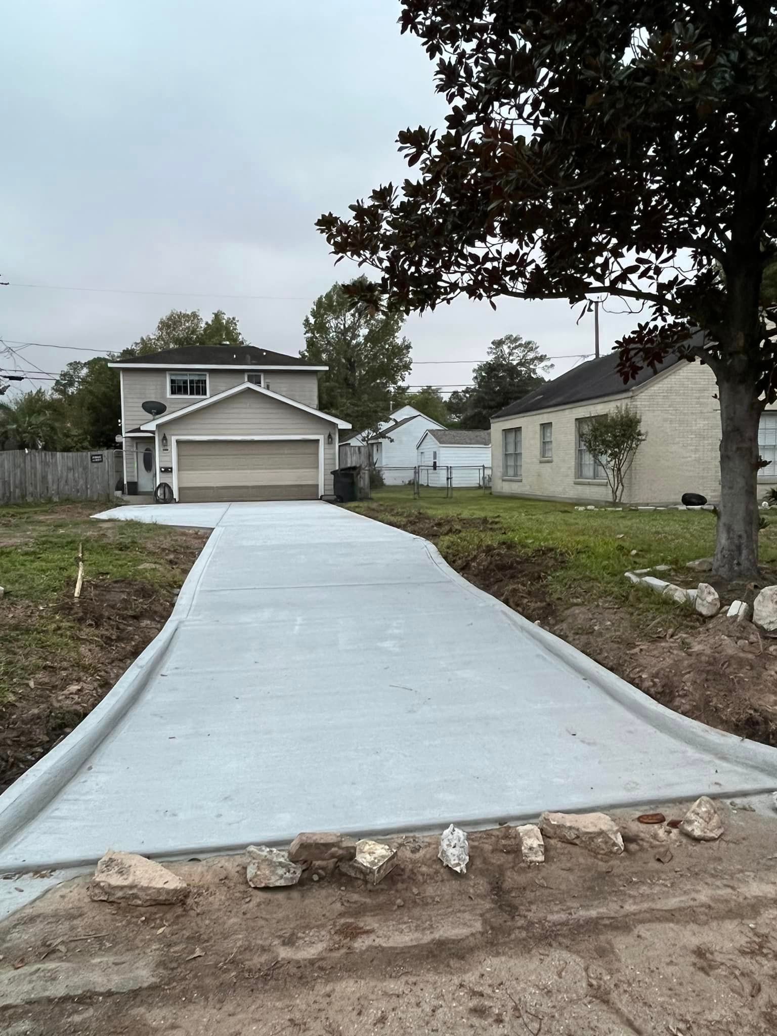Newly poured concrete driveway leading to a two-car garage under a cloudy sky.