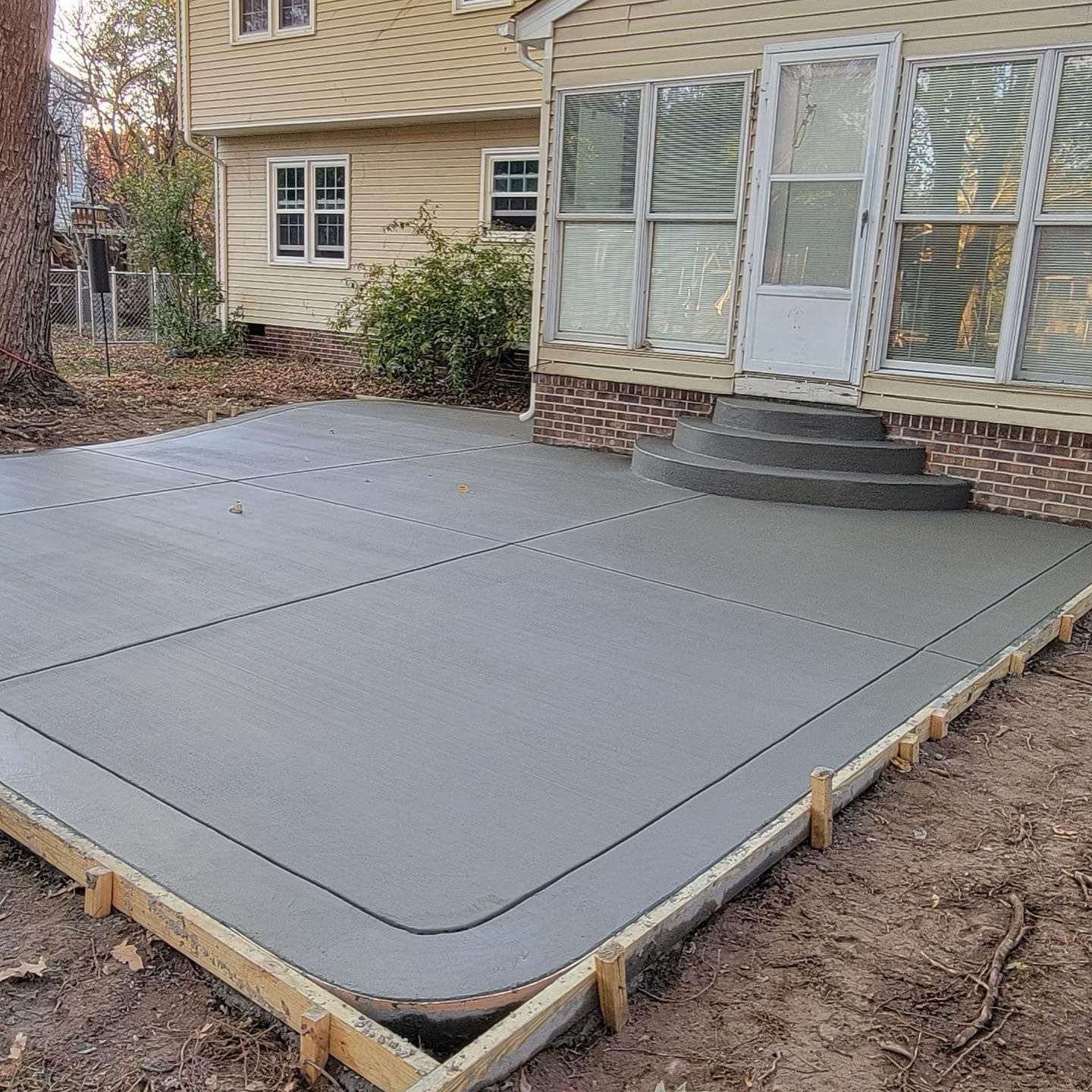 Newly poured concrete patio next to a brick house with a sunroom and steps.