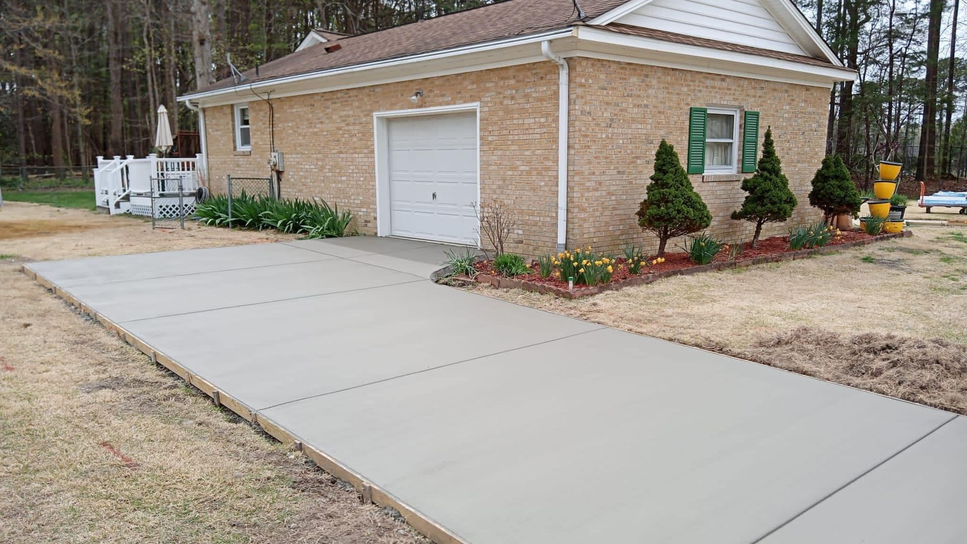 New concrete driveway leading to a brick garage with green shutters and landscaping.