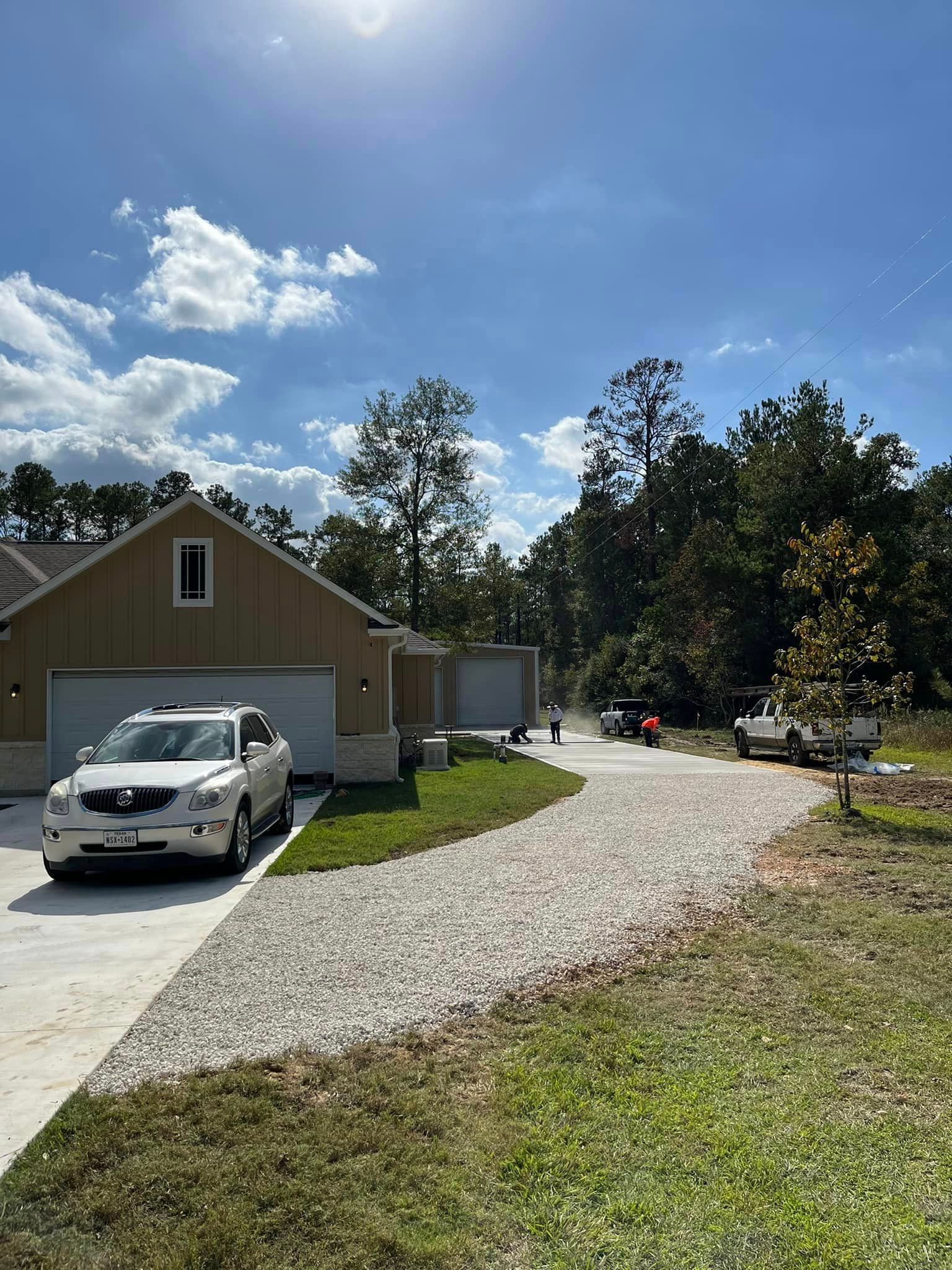 SUV parked on gravel driveway in front of a tan house with attached garage on a sunny day.