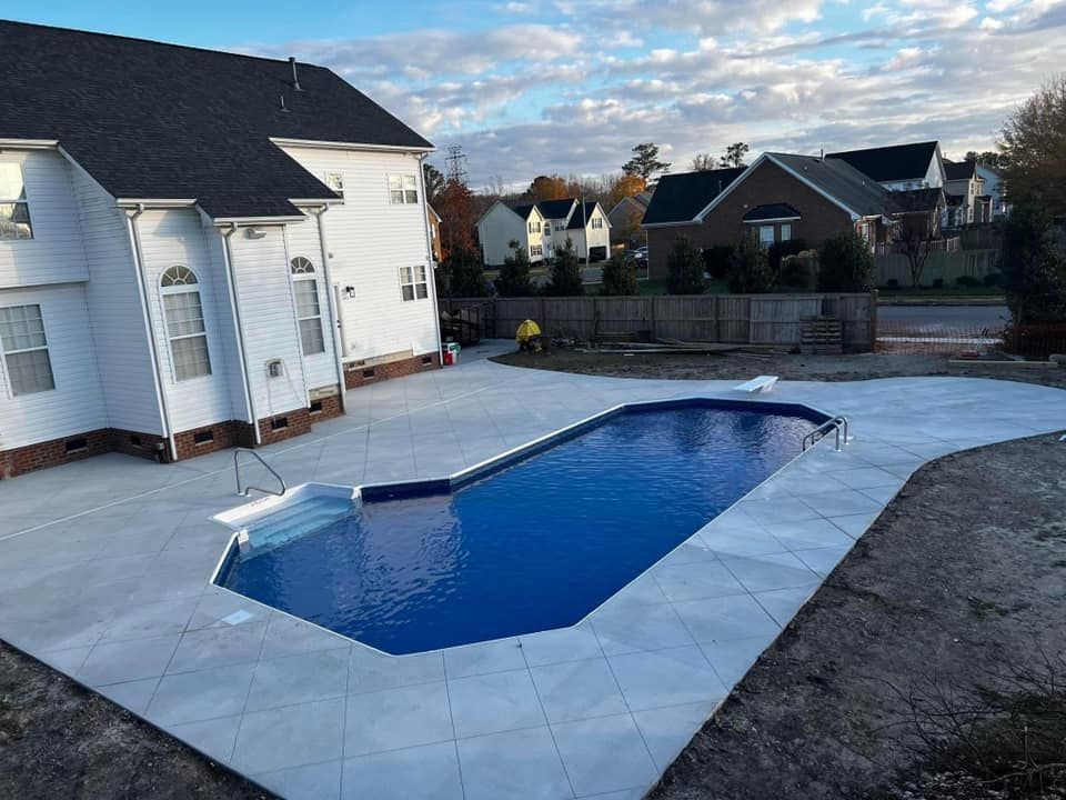 Backyard with new blue pool and light gray patio; white house in the background.