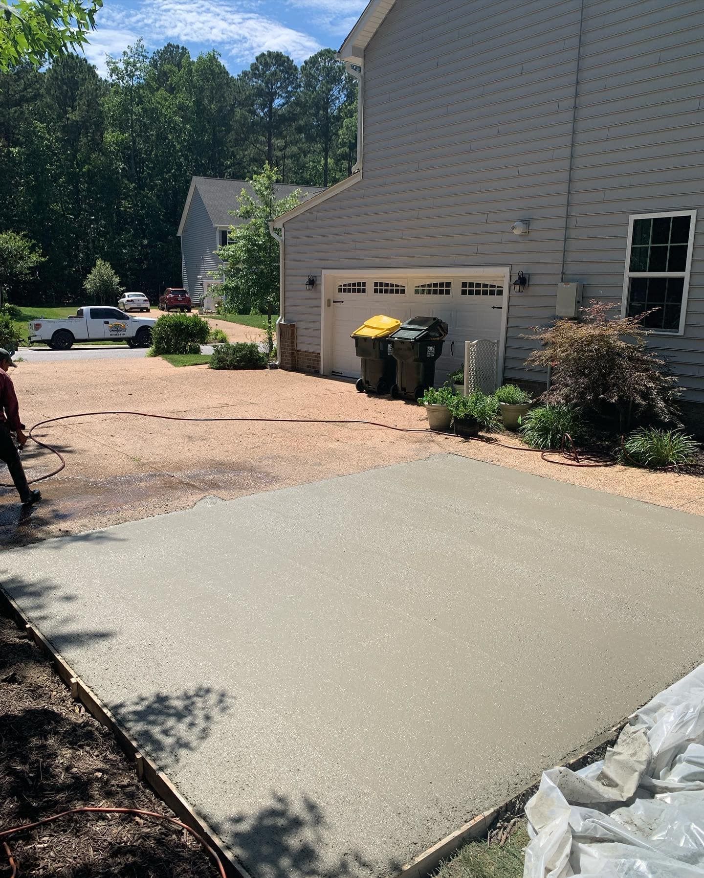 Freshly poured concrete driveway; construction site. Gray cement contrasts with gravel. Trash cans beside garage.