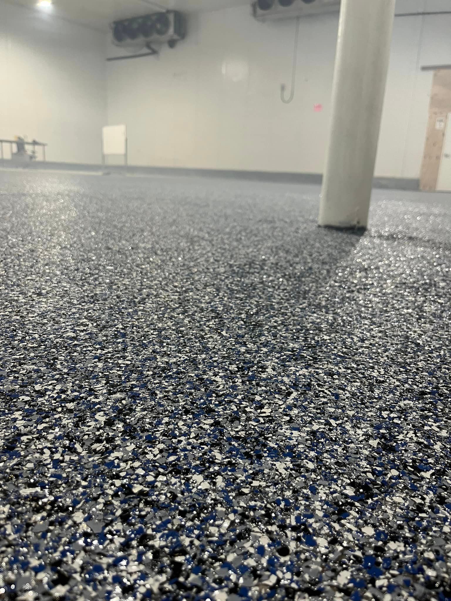 Blue, white, and black speckled epoxy floor in a commercial setting with a white column and freezer units.