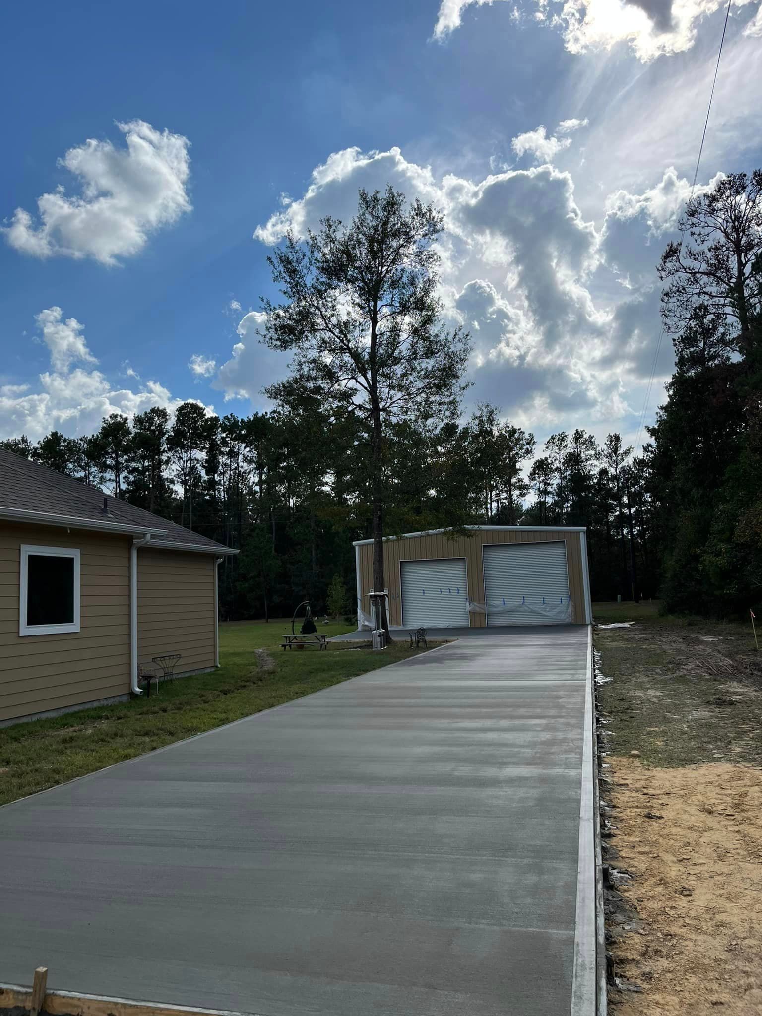 A freshly poured concrete driveway leading to a two-car garage under a partly cloudy blue sky.