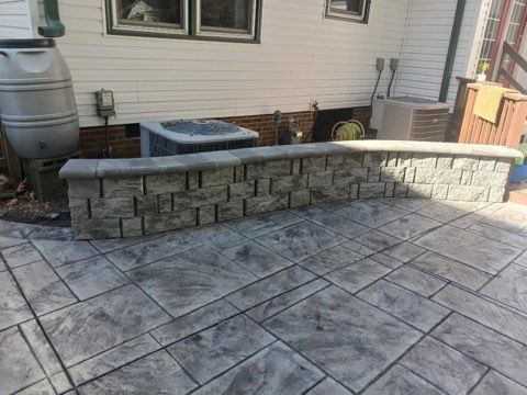 Gray stone patio with a low retaining wall, near a house with rain barrel and air conditioning units.