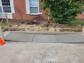 New concrete sidewalk sections in front of a brick house, with caution tape.