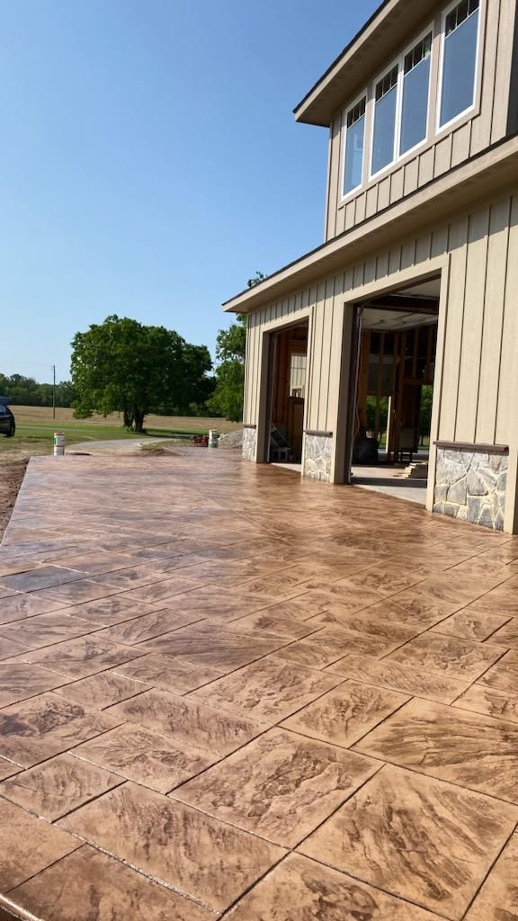 Brown stamped concrete patio next to a two-story house with an open garage. Sunny day.