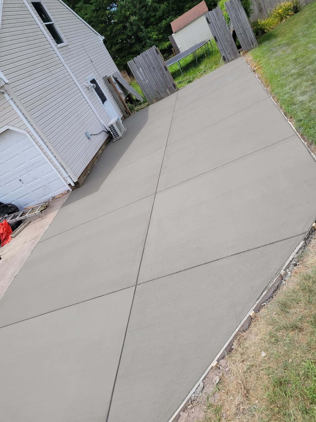 Newly poured gray concrete driveway next to a house and yard, with saw cuts for expansion.