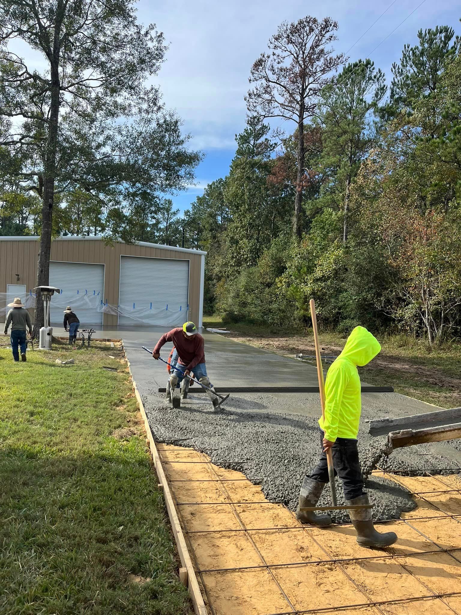 Construction workers paving a driveway with fresh concrete. One worker in a neon jacket walks with a tool.