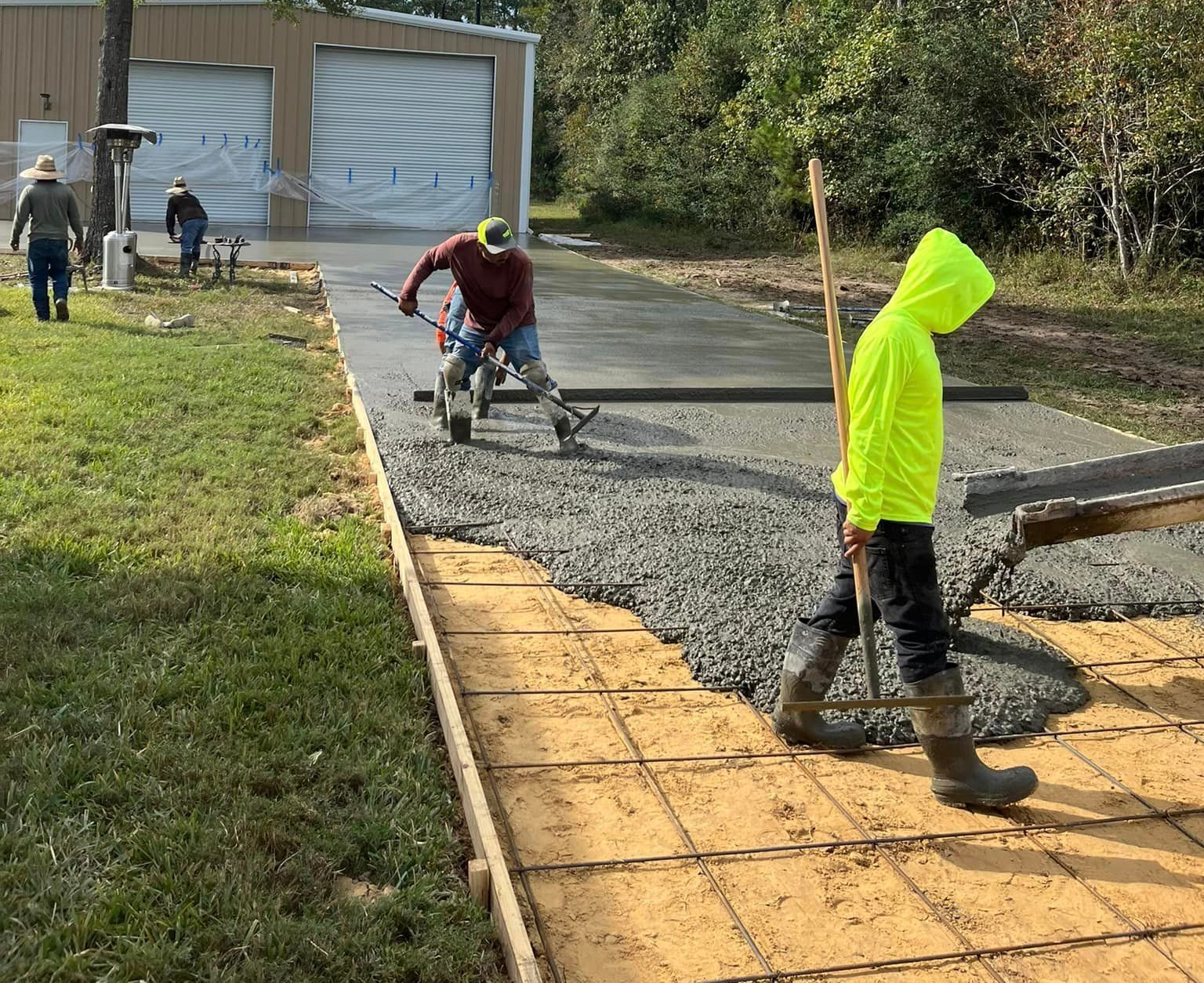 Construction workers pouring concrete driveway outside a garage.