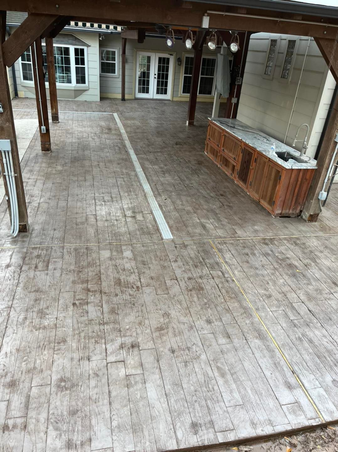 Stained concrete patio with a bar, covered by a wooden pergola. Beige and brown colors.