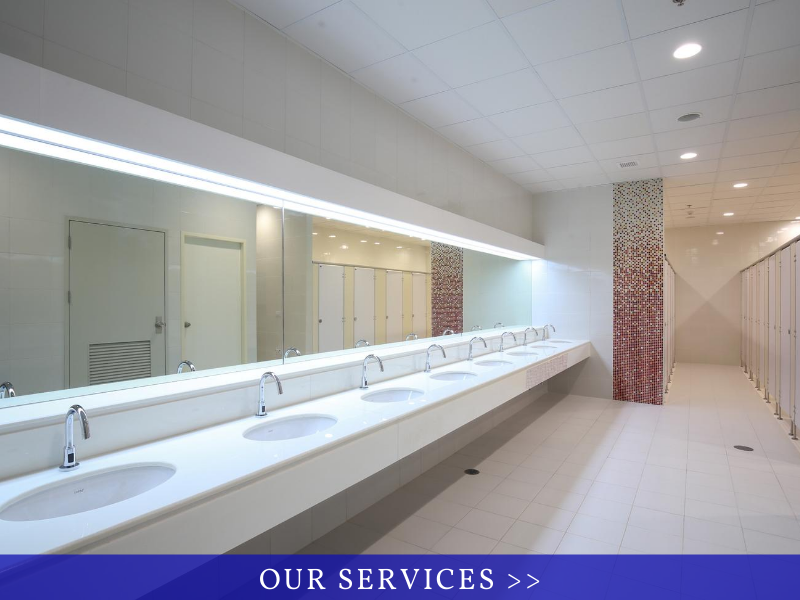 Modern public restroom with long row of white sinks and mirrors under bright ceiling lights