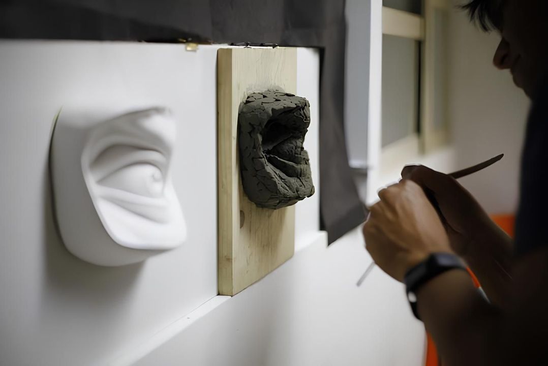 Persona che scolpisce un occhio in argilla su una tavola, indossando una maschera, in un laboratorio.