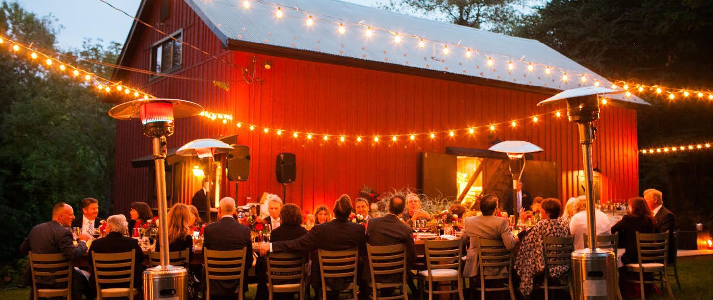 a group of people are sitting at tables in front of a red barn