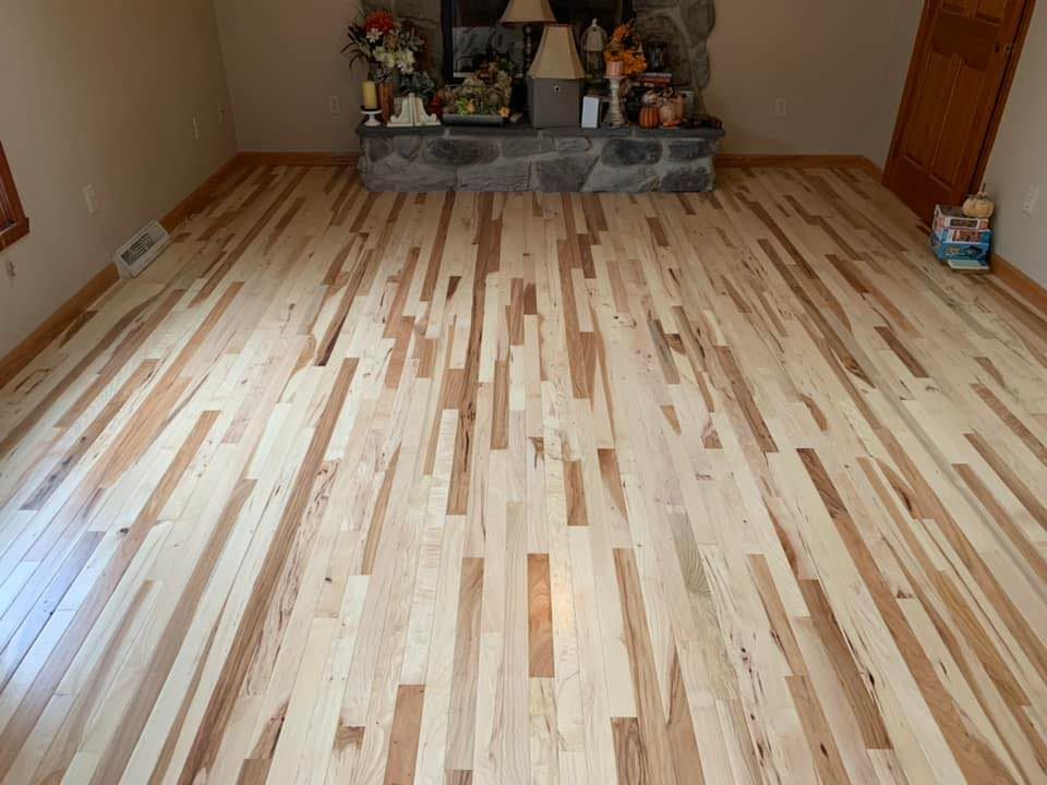 Room with newly installed light wood flooring and a fireplace alcove at the far end.