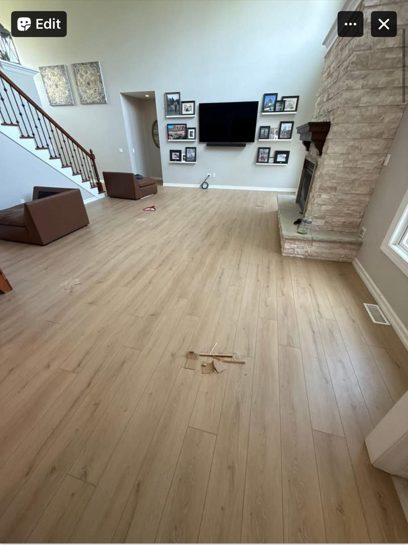Spacious living room with light wood floors, wall-mounted TV, staircase, and stone fireplace.