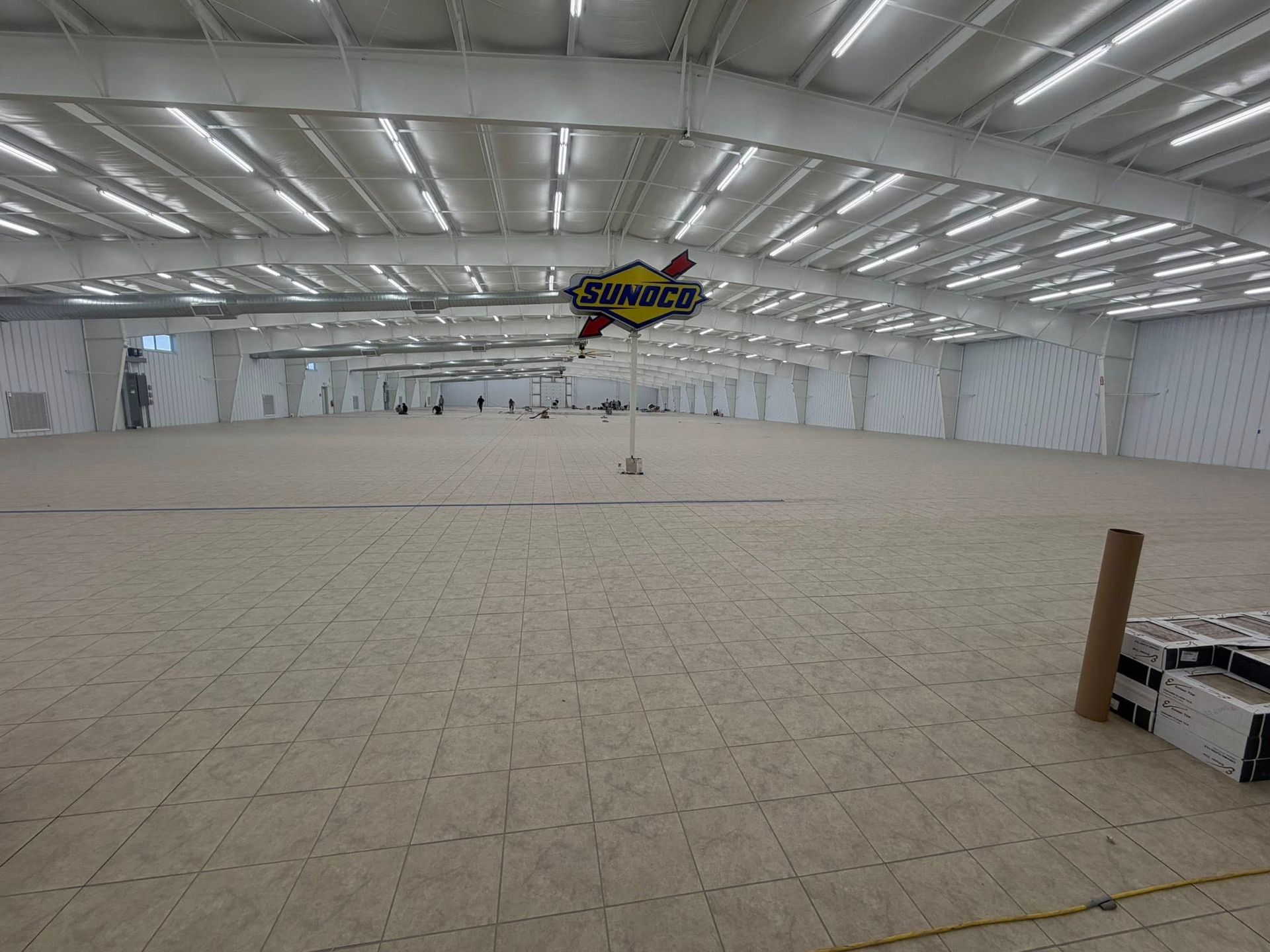 Empty indoor arena with bright ceiling lights and tiled floor, a sign hanging near the center.