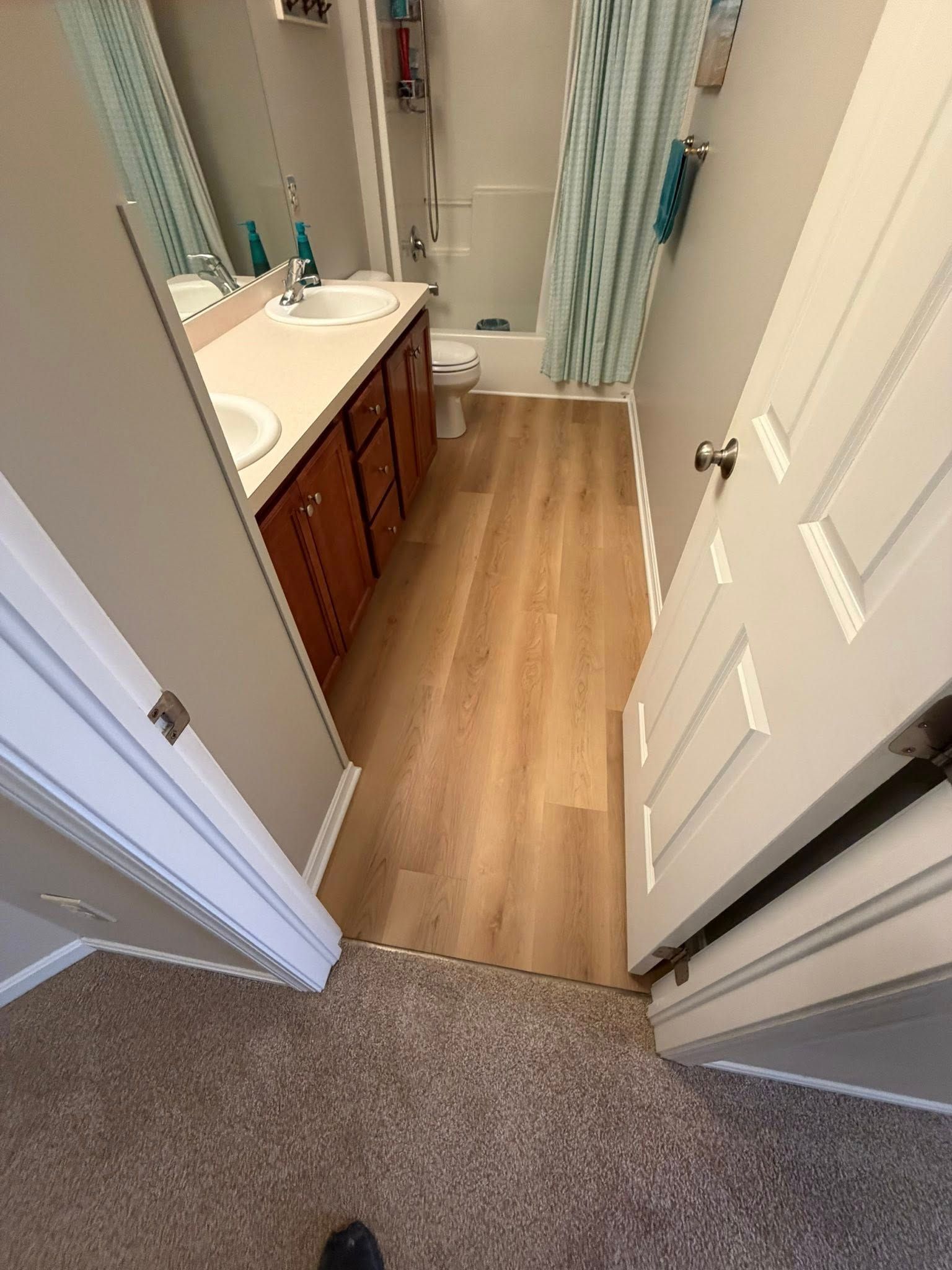 Small bathroom viewed from doorway, with white sink, wood vanity, blue-striped shower curtain, and wood floor.