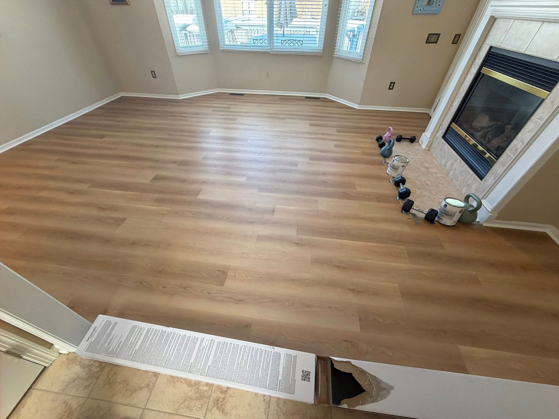 Empty living room with light wood floors, fireplace, and windows letting in daylight.