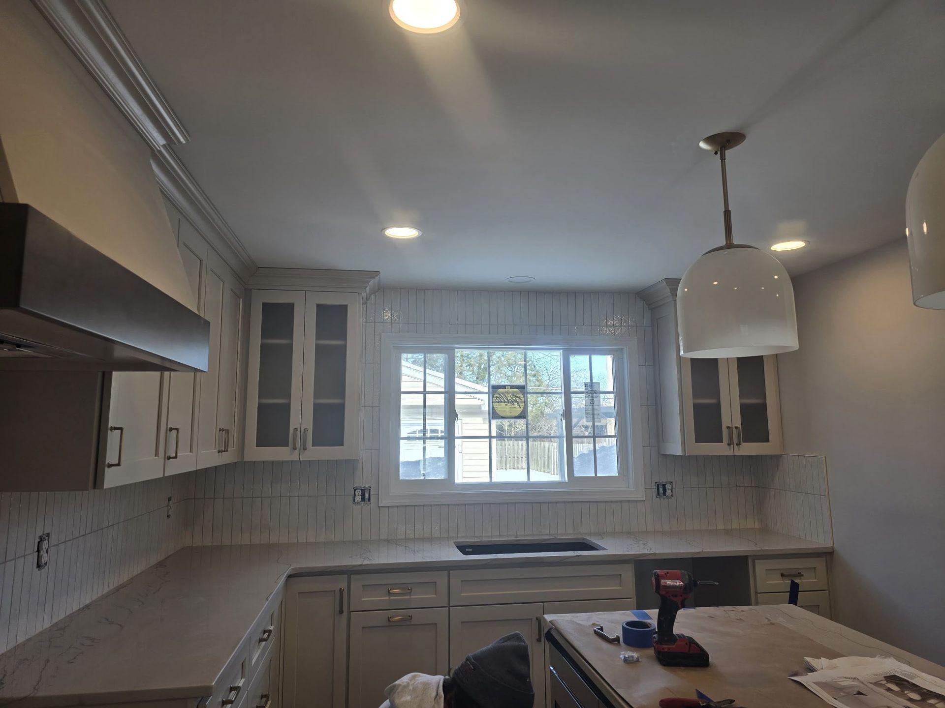 Bright kitchen with white cabinets, tiled backsplash, window, and a central island under pendant lights