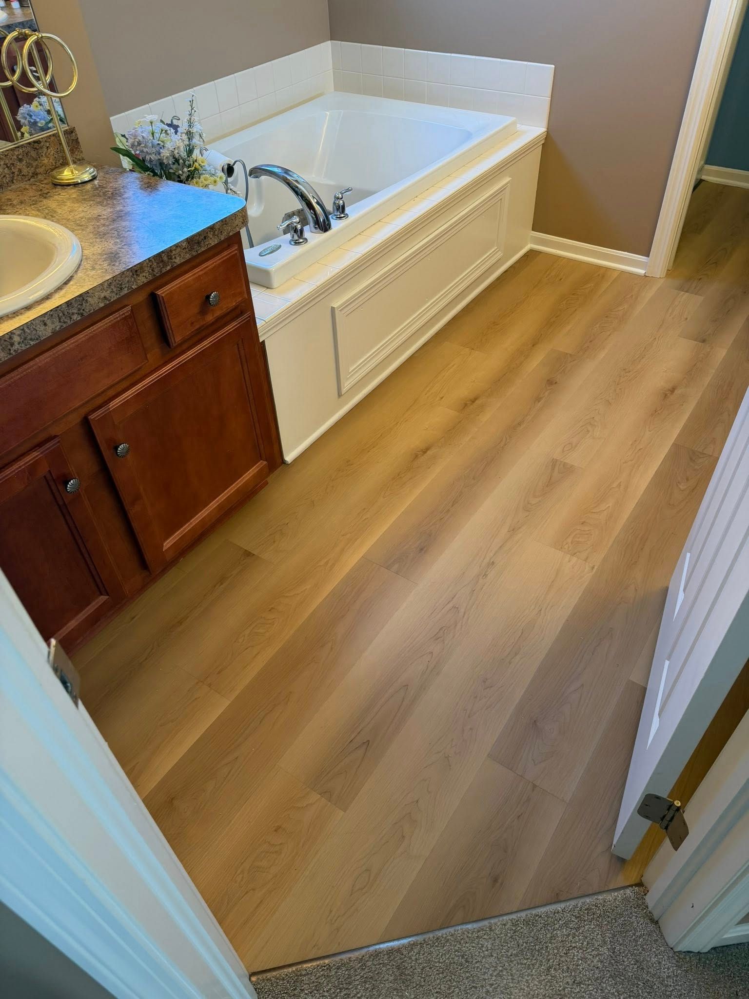 Bathroom with wood-look floor, white tub, and wooden vanity.