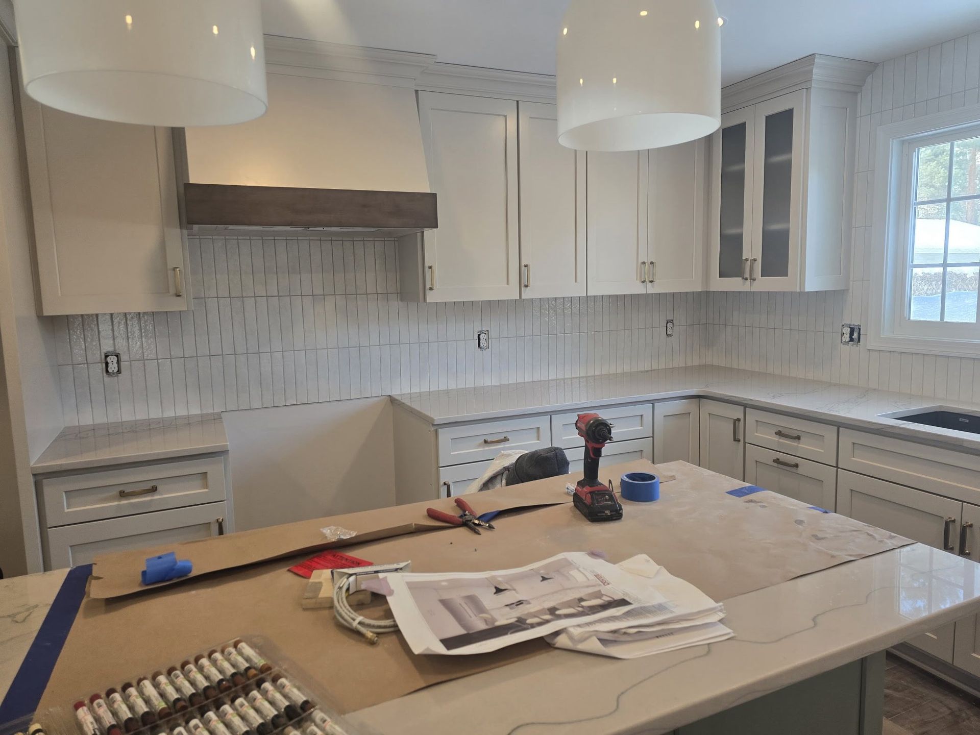 Bright white kitchen under renovation with tools and papers on a marble island and pendant lights overhead