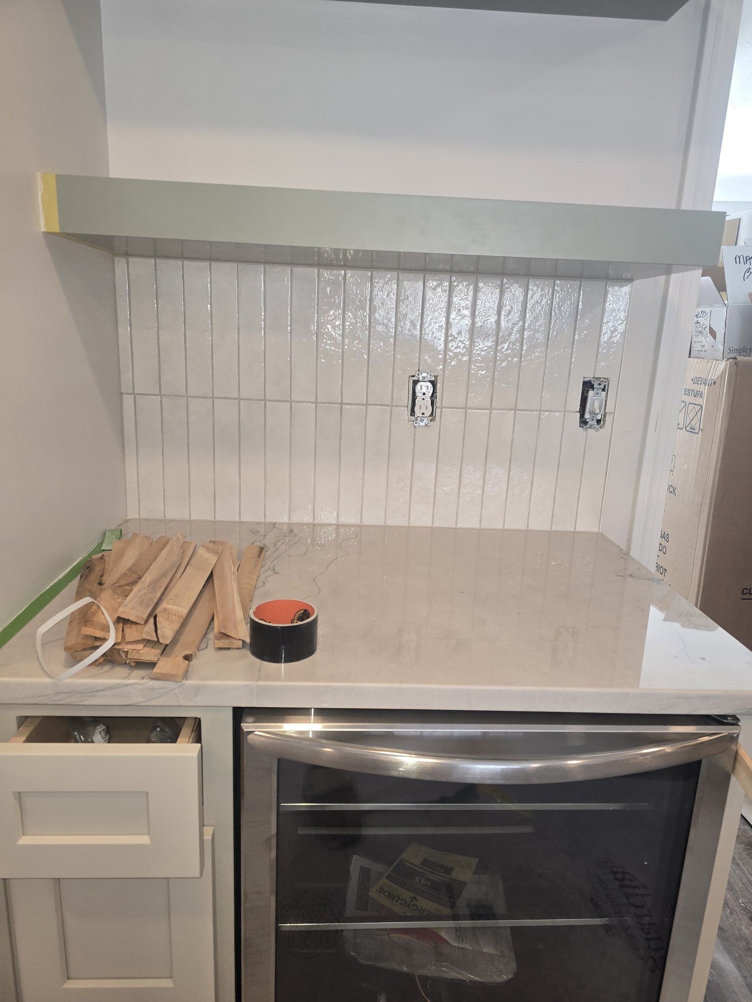Kitchen countertop with unfinished backsplash tile, wooden slats, and a tape measure beside a stove oven.