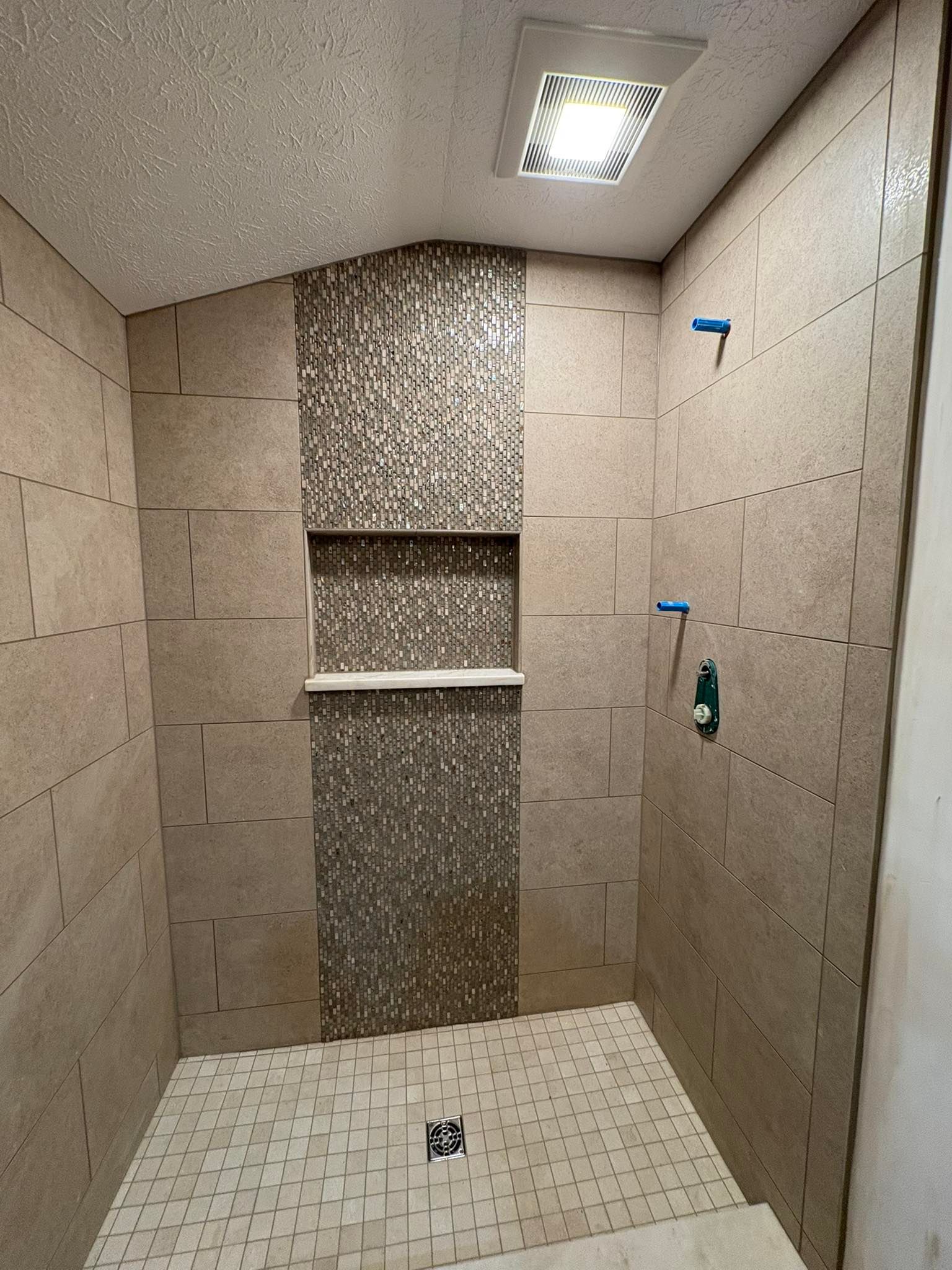 Empty tiled shower stall with built-in shelf, two wall fixtures, and a ceiling light