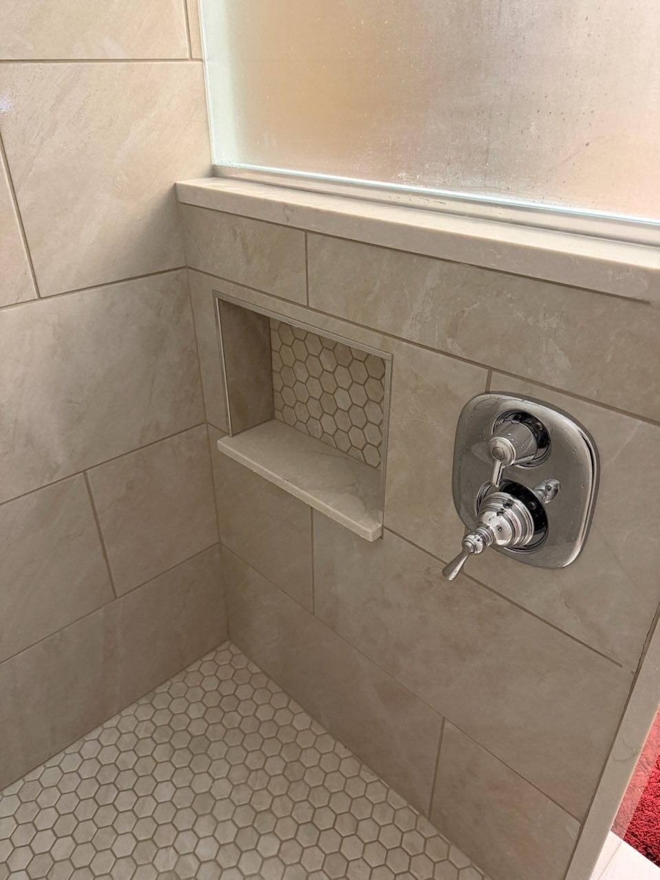 Tiled shower corner with built-in shelf, window ledge, and chrome shower valve.