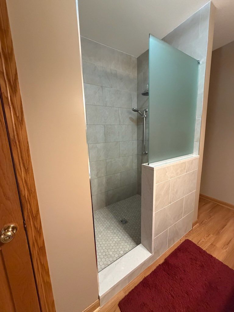 Bathroom shower stall with frosted glass door and tiled walls beside a red rug