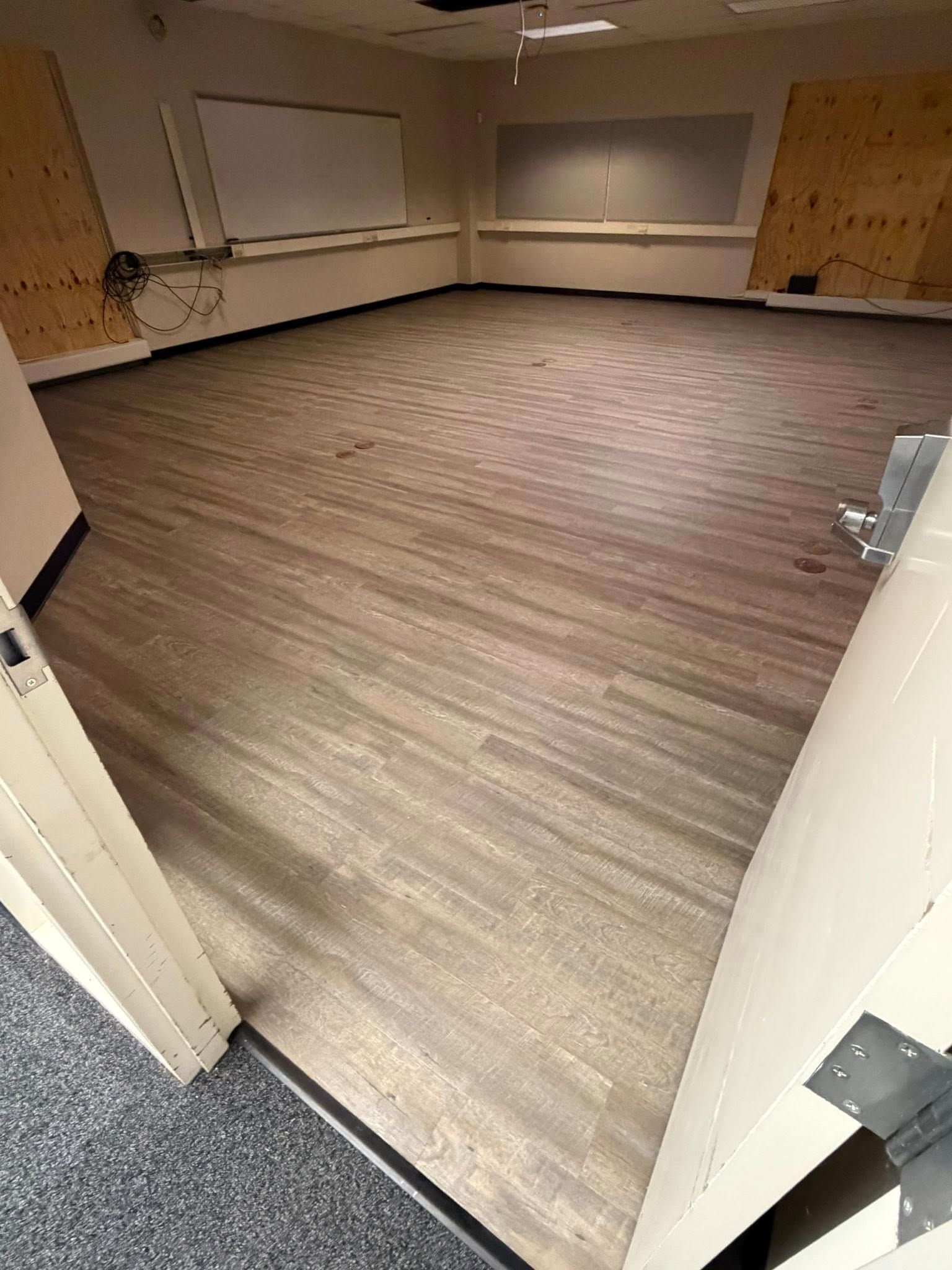 Empty room with wood-look flooring, beige walls, windows, and a gray carpeted entryway