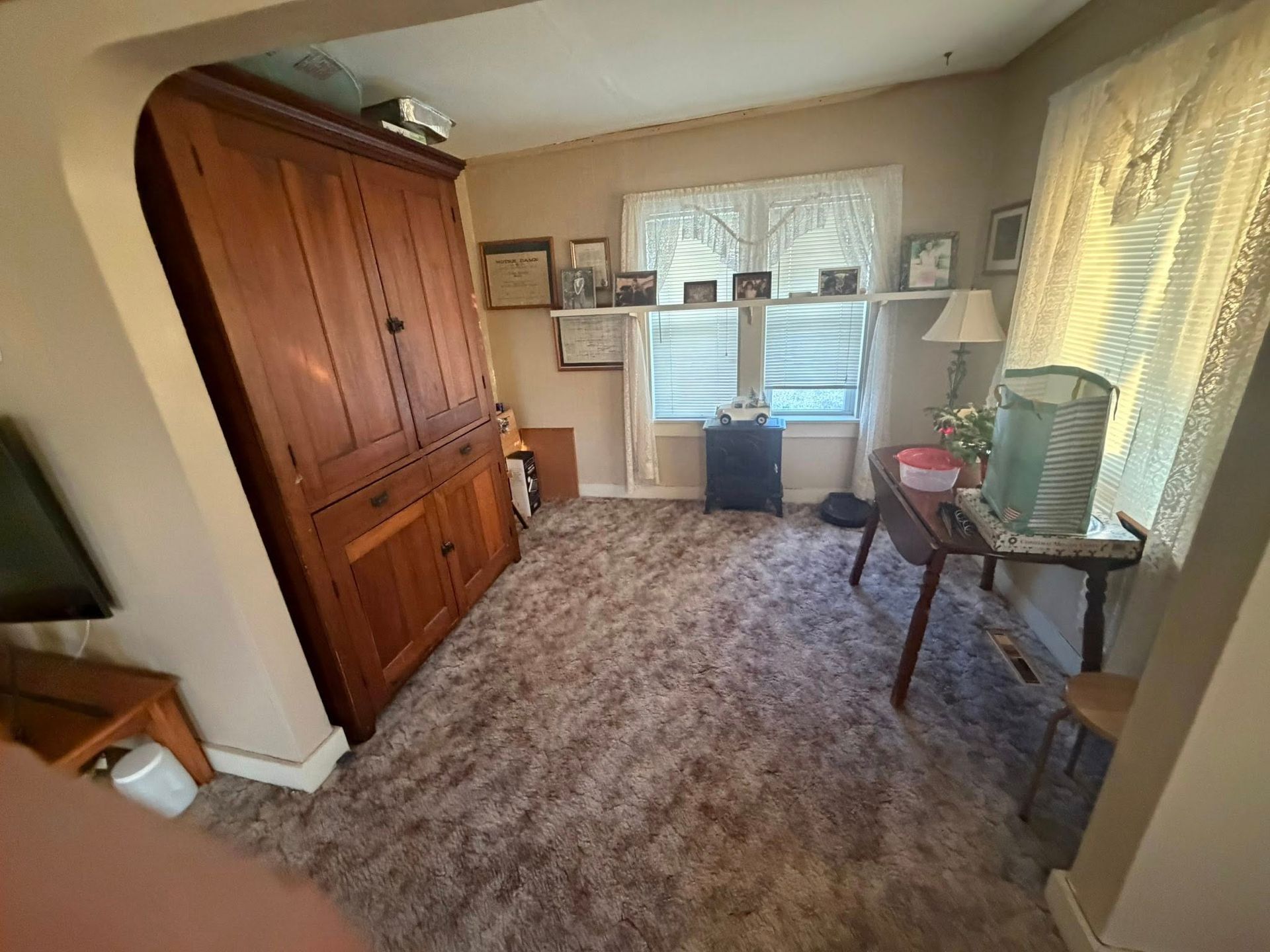 Small bedroom with carpet, wooden wardrobe, desk, and window with blinds and curtains