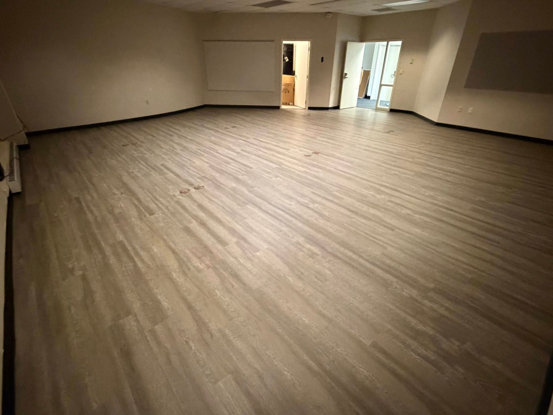Empty beige room with wood-look flooring and open doorways at the back