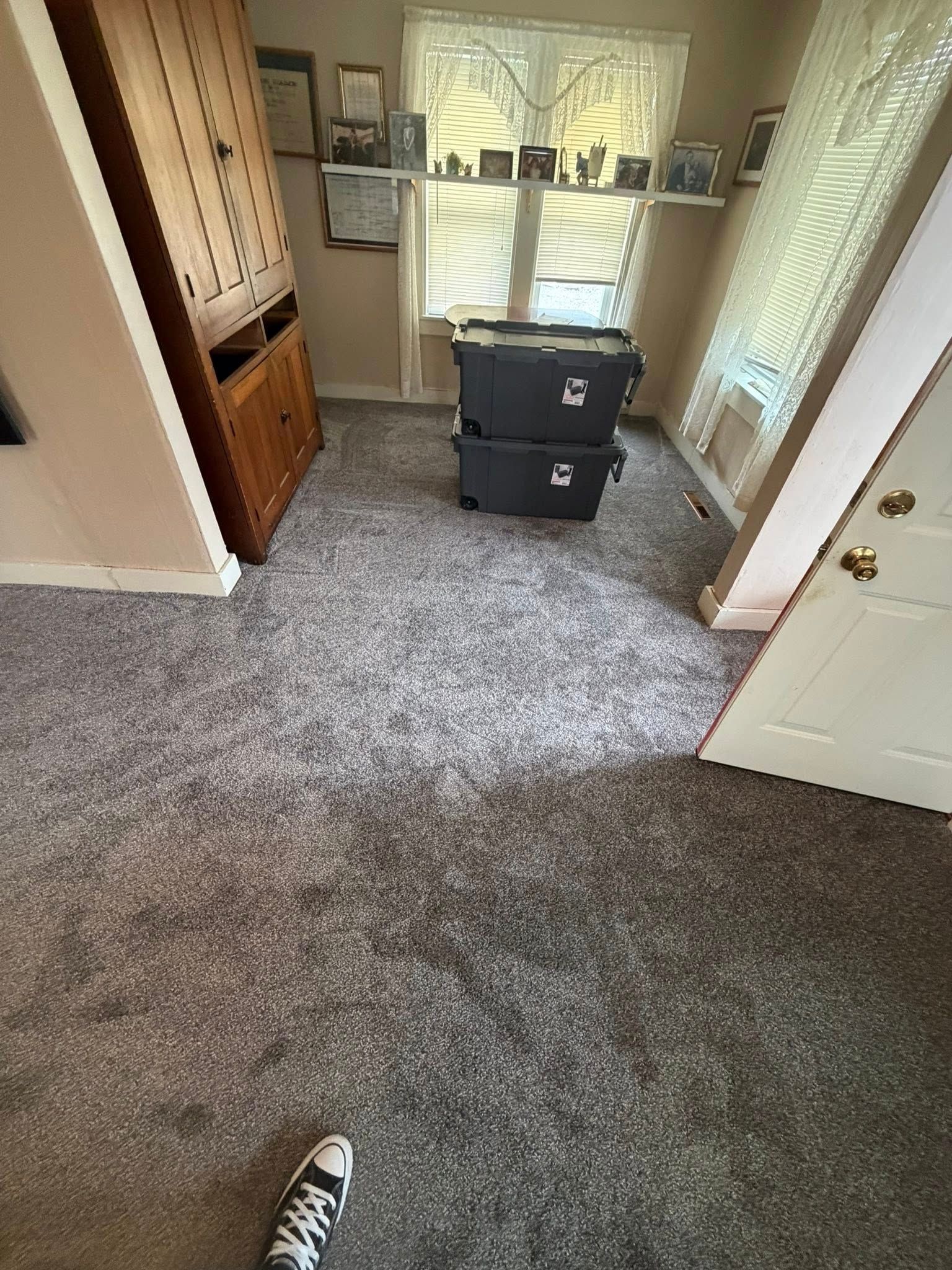 Carpeted bedroom with two black storage bins, open closet, and window light.