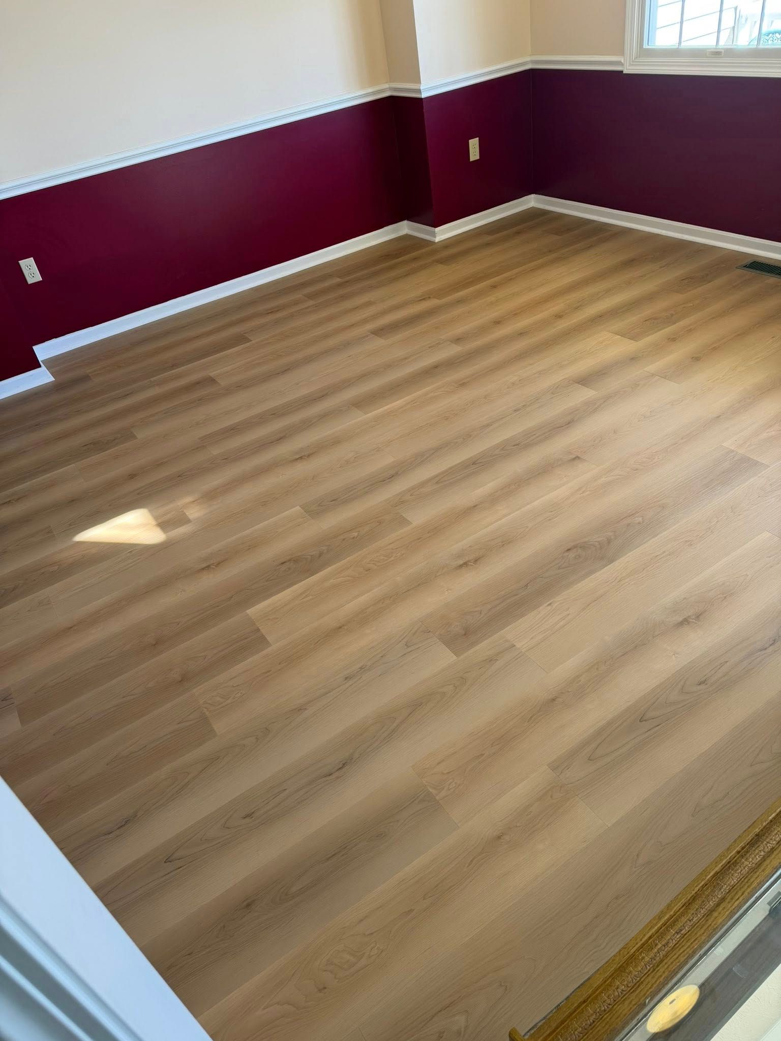 Empty room with light wood flooring, maroon walls, and white trim.