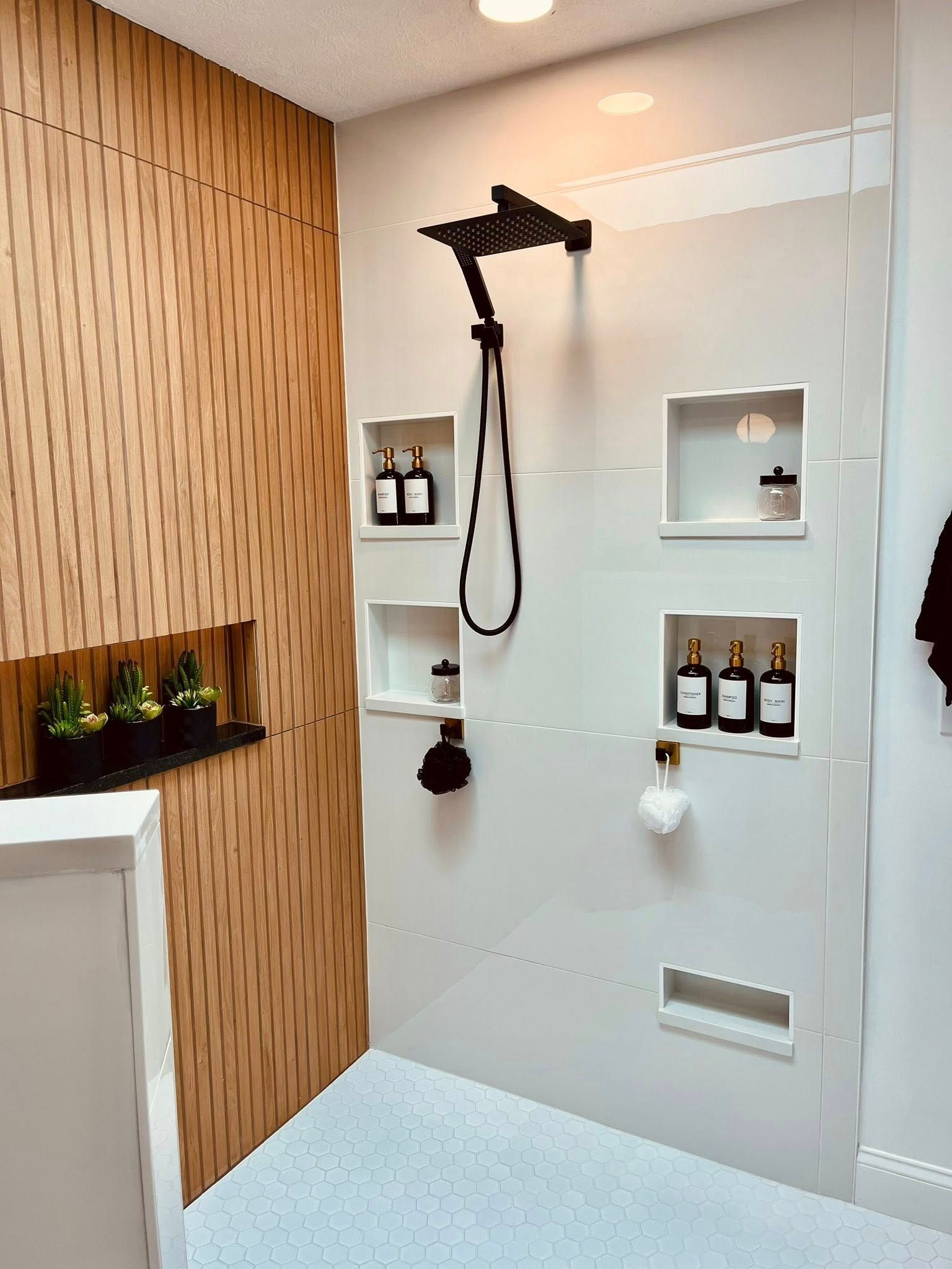 Modern shower with white tiled wall, black showerhead, built-in niches, and wood accent paneling