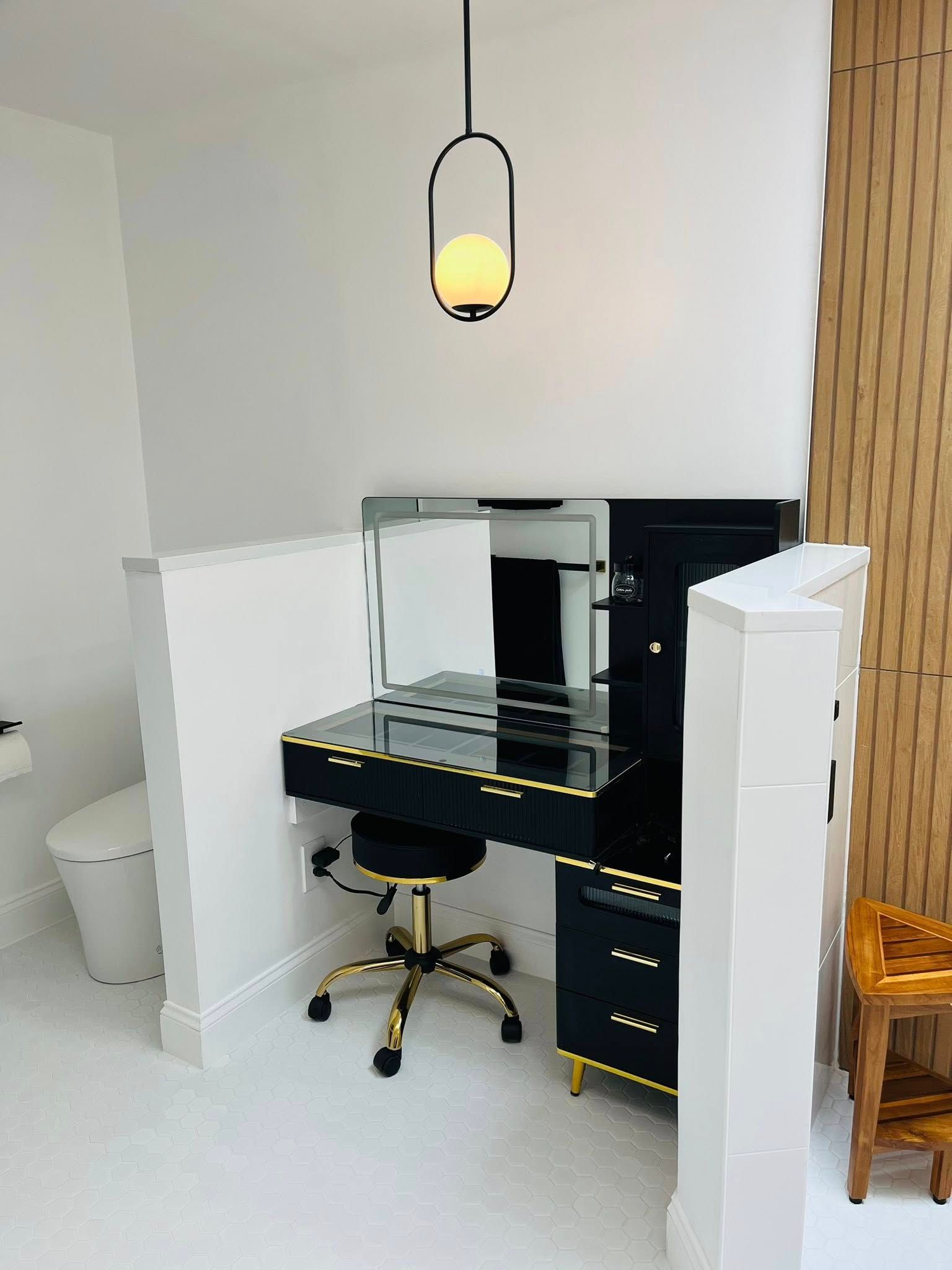 Black desk with mirror, chair, and hanging light in a white room