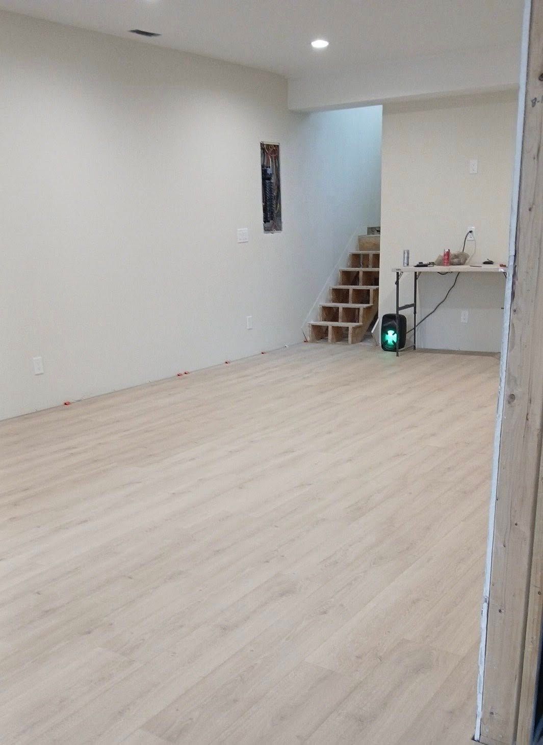 Empty white room with light wood flooring, stairs in back, and a small table by the wall