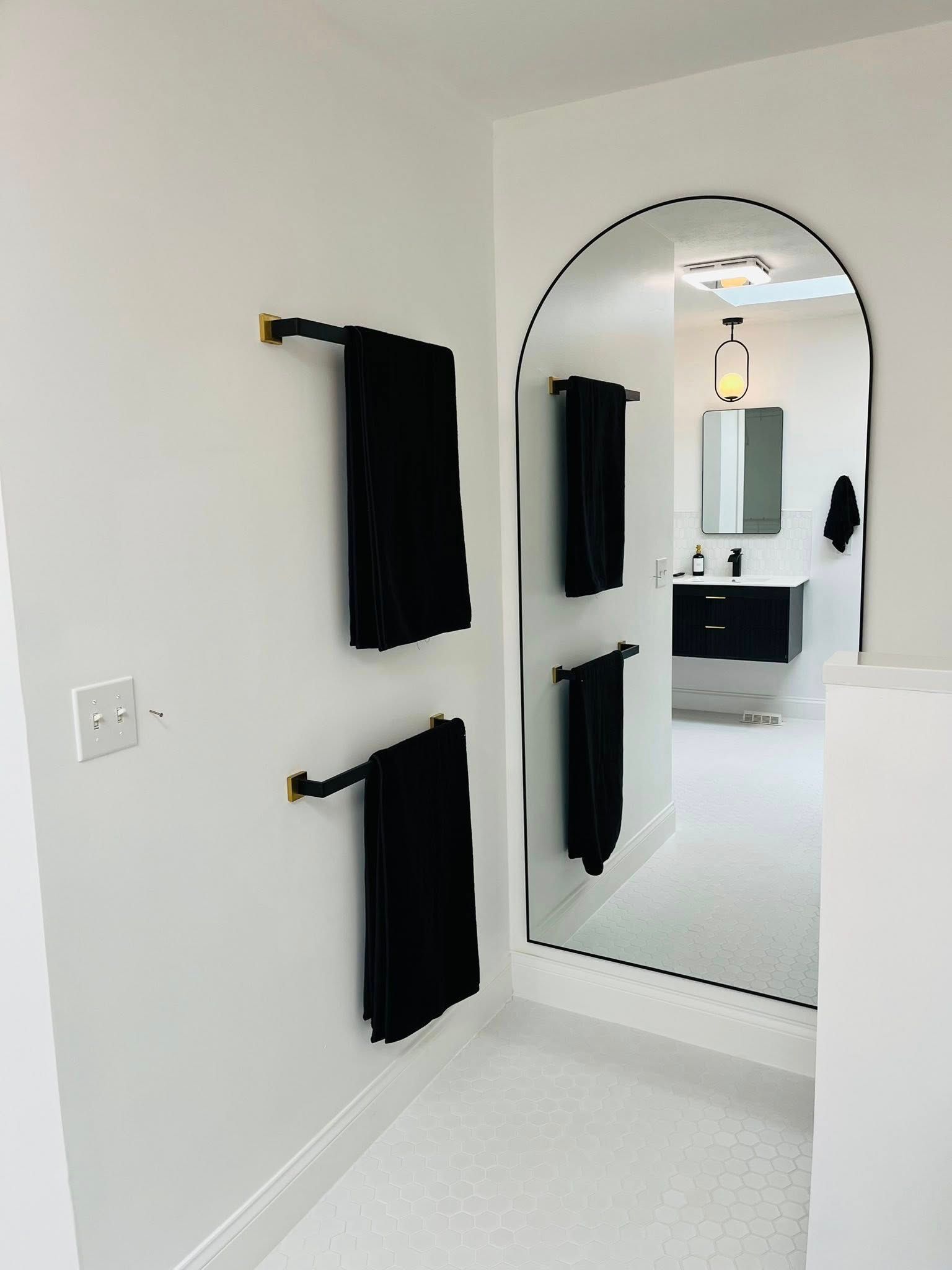Minimal white bathroom with black towels and a tall arched mirror reflecting the sink area