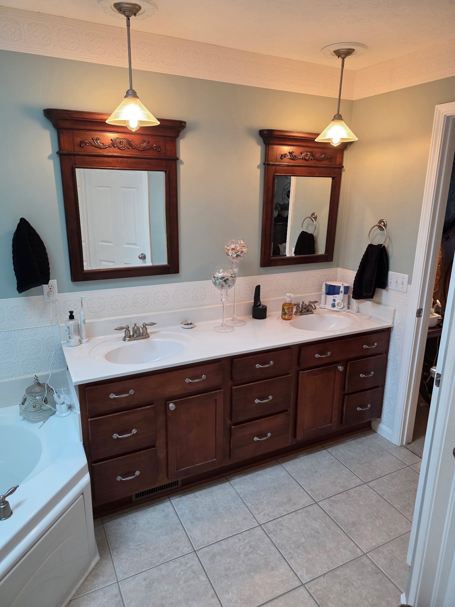 Bathroom vanity with double mirrors, wood cabinets, white countertop, and warm pendant lights.