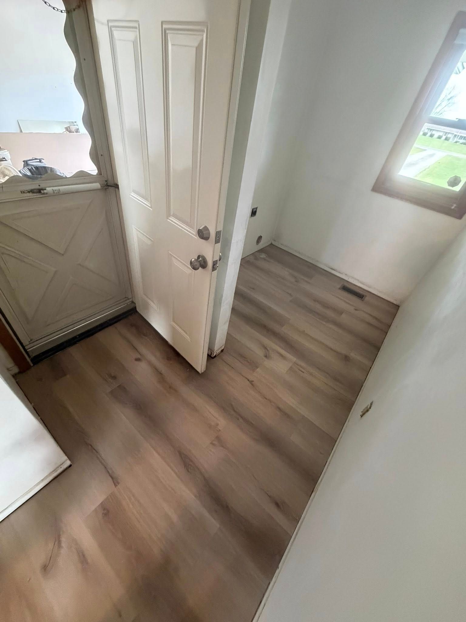 Small empty room with wood floor, white walls, open door, and a window on the right.