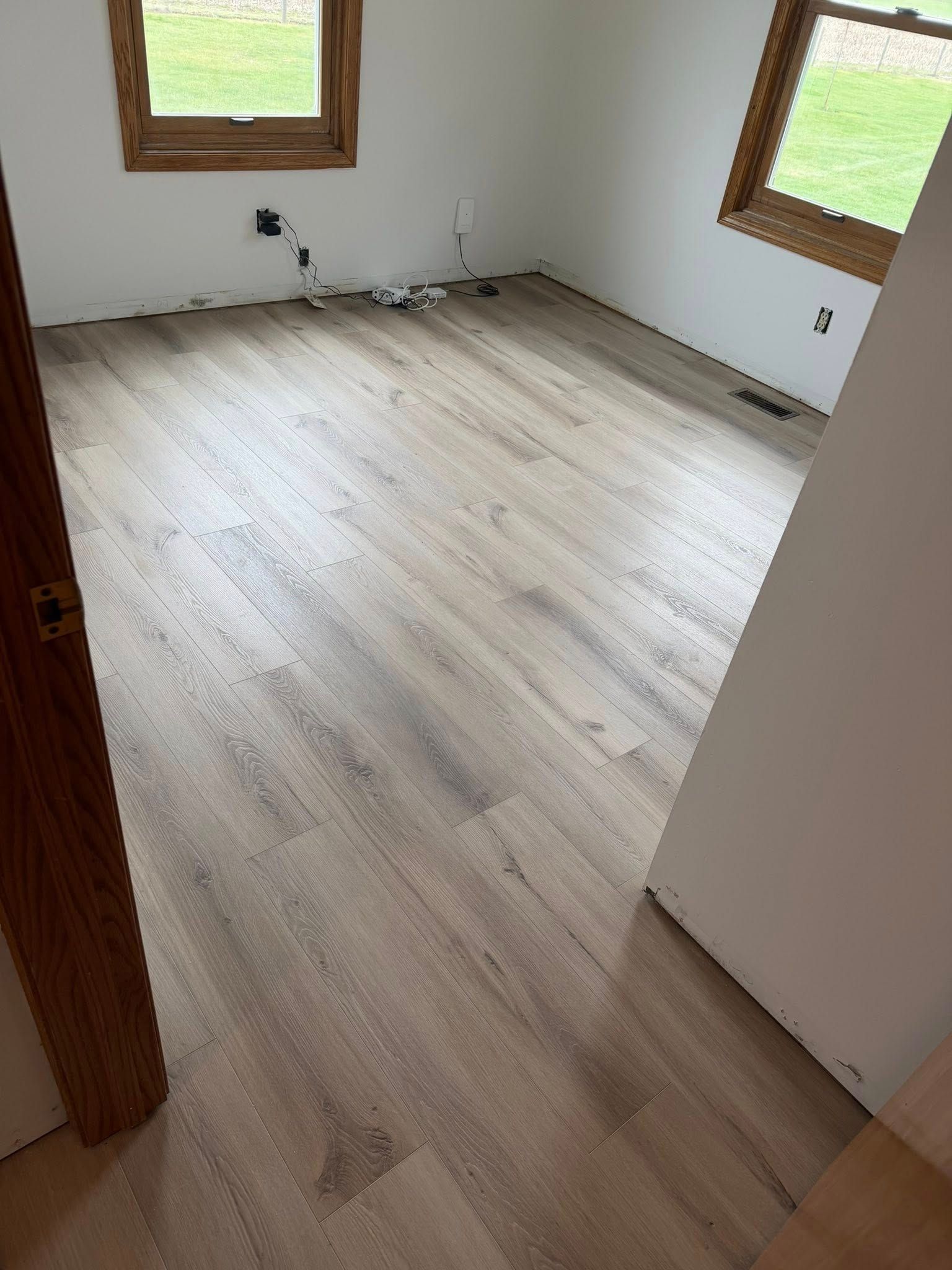 Empty room with light wood flooring, white walls, and two windows with wooden trim.