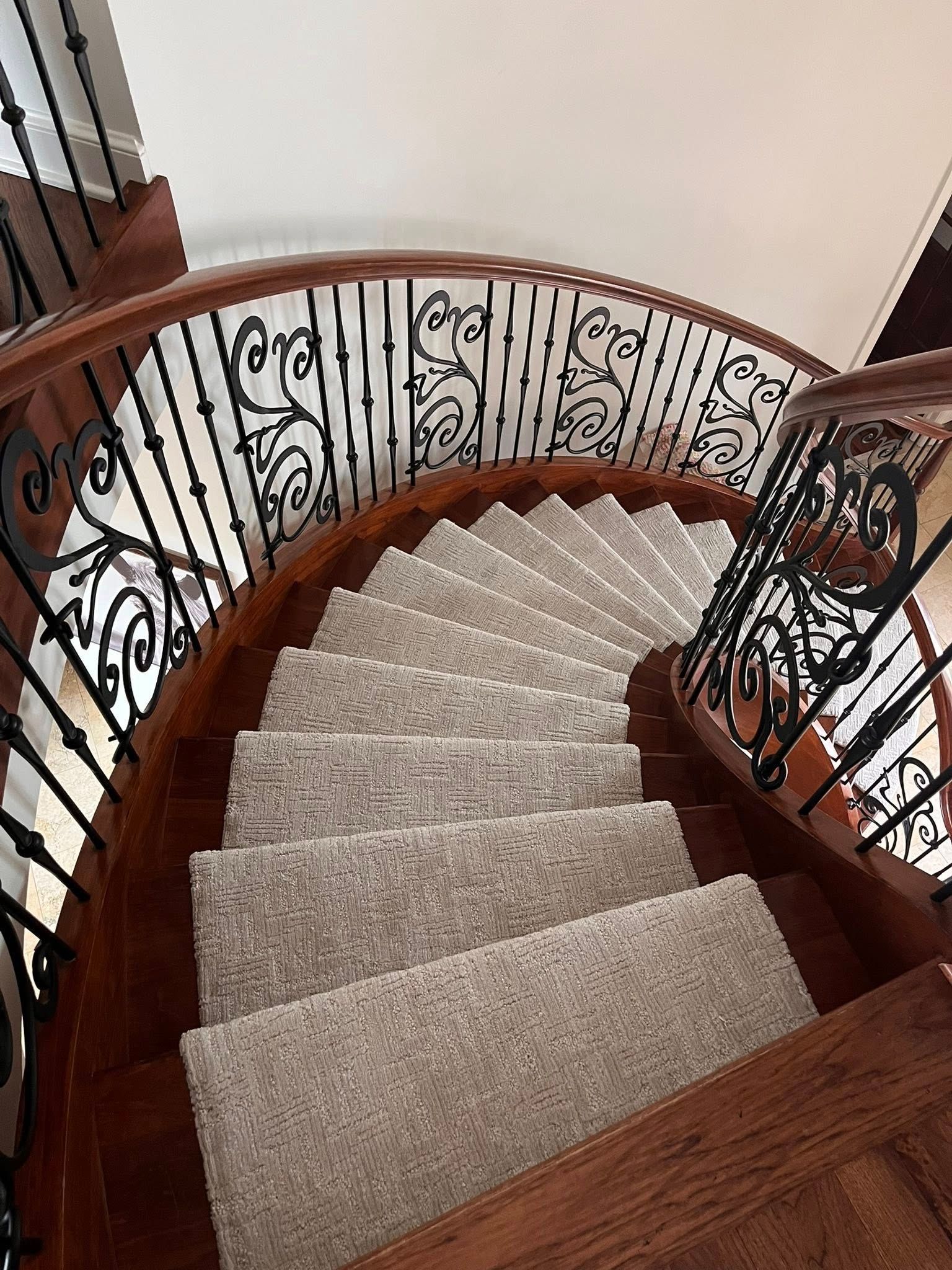 Curved carpeted staircase with dark wood steps and ornate black railing in a home