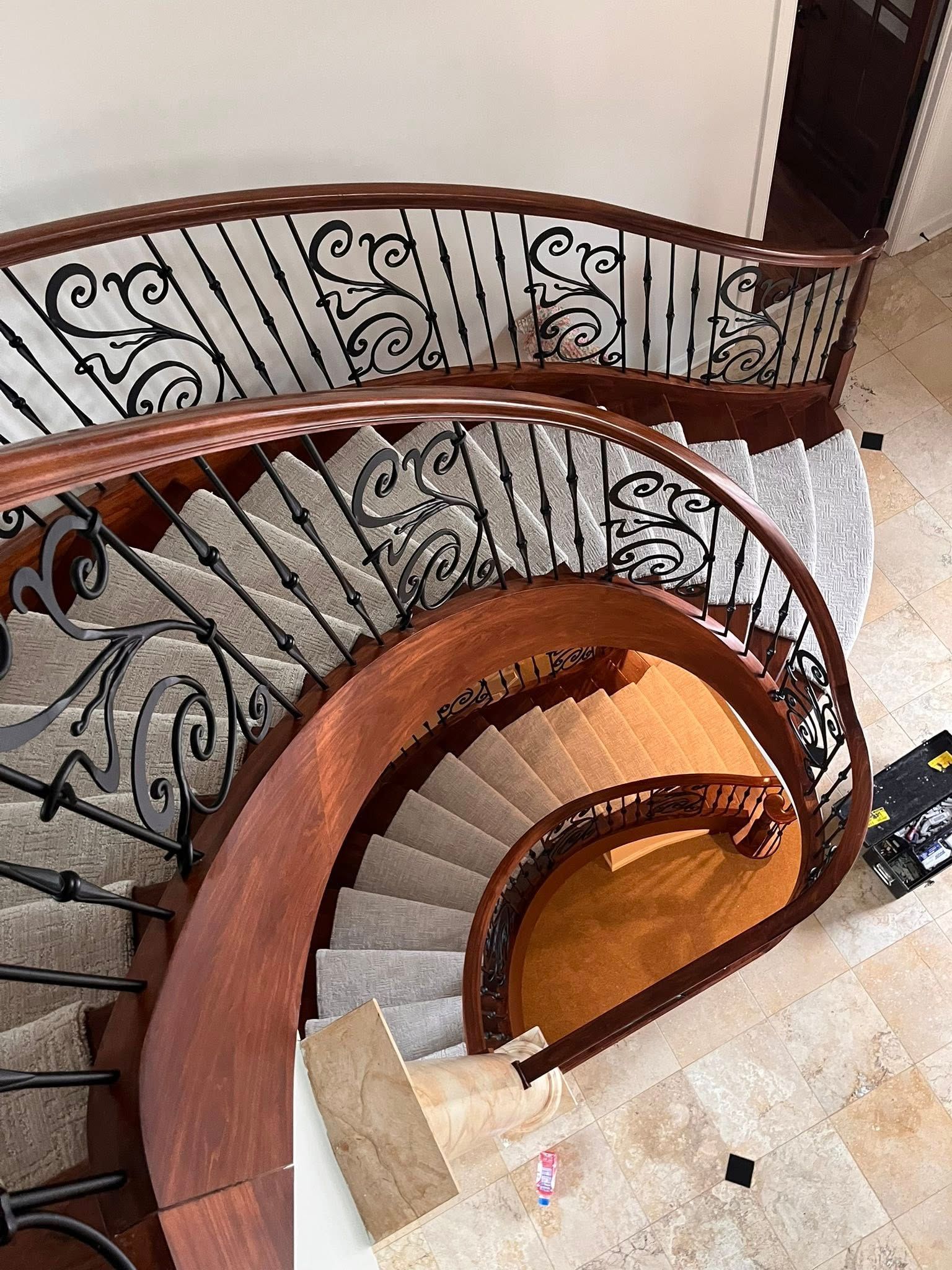 Curved wooden staircase with ornate black iron railing in a bright interior